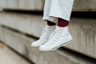 Crop unrecognizable person in stylish sneakers sitting on concrete beam