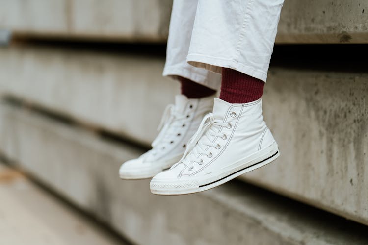 Crop Unrecognizable Person In Stylish Sneakers Sitting On Concrete Beam