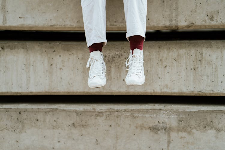 Crop Faceless Person In Gumshoes Sitting On Dirty Cement Beams