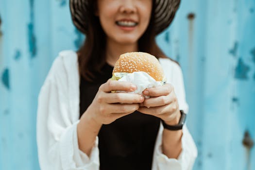 A joyful woman holding a sesame seed hamburger, smiling in a casual outdoor setting.
