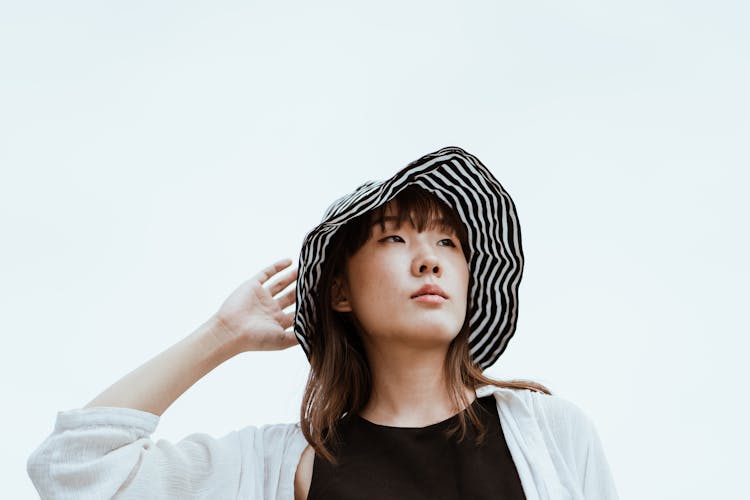 Dreamy Asian Woman In Hat Touching Head On Blue Background