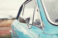 Old blue retro car after rain parked in countryside against cloudy sky in overcast weather