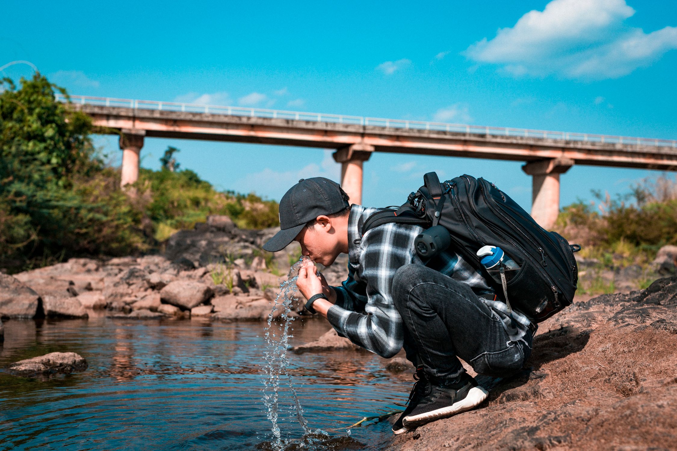 Backpacker squatting by the water's edge during a coastal trekking expedition Backpacker squatting by the water's edge during a coastal trekking expedition