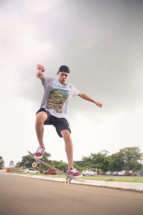 From below of fit male athlete jumping with skateboard above asphalt roadway under cloudy sky in city