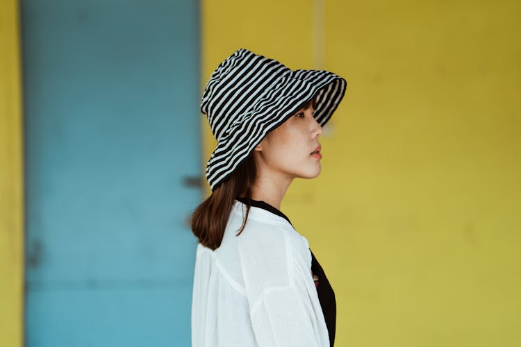 Pensive Woman In Striped Hat Standing Near Yellow Wall