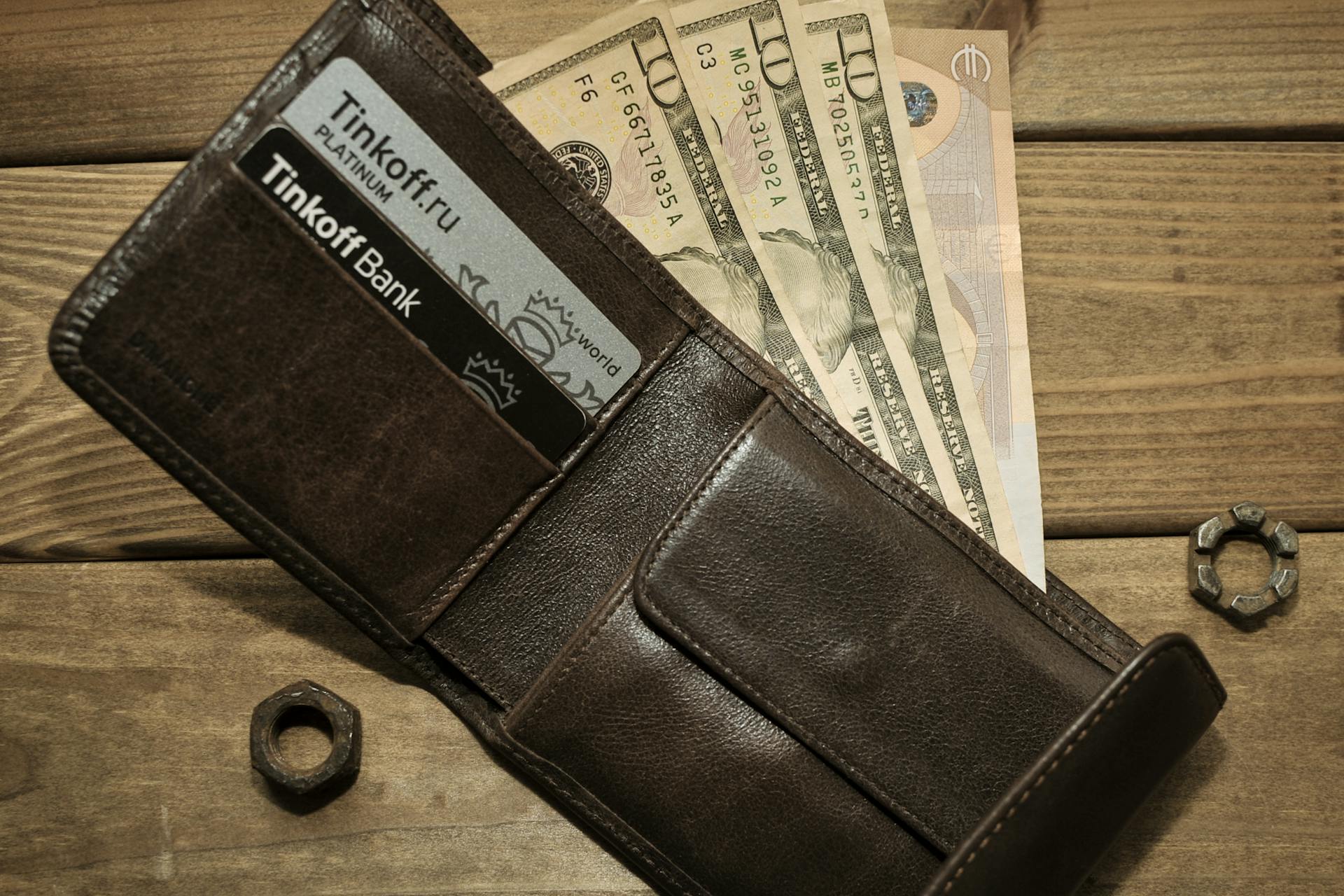 Brown leather wallet open with Tinkoff Bank cards visible alongside US dollars.