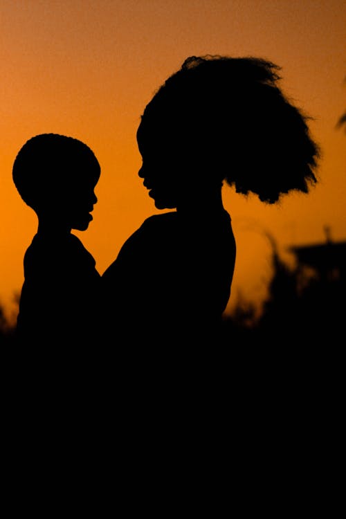 Silhouette Photo of Mom and Child Against Orange Background