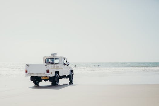A lifeguard vehicle on a peaceful beach with people swimming in the ocean.