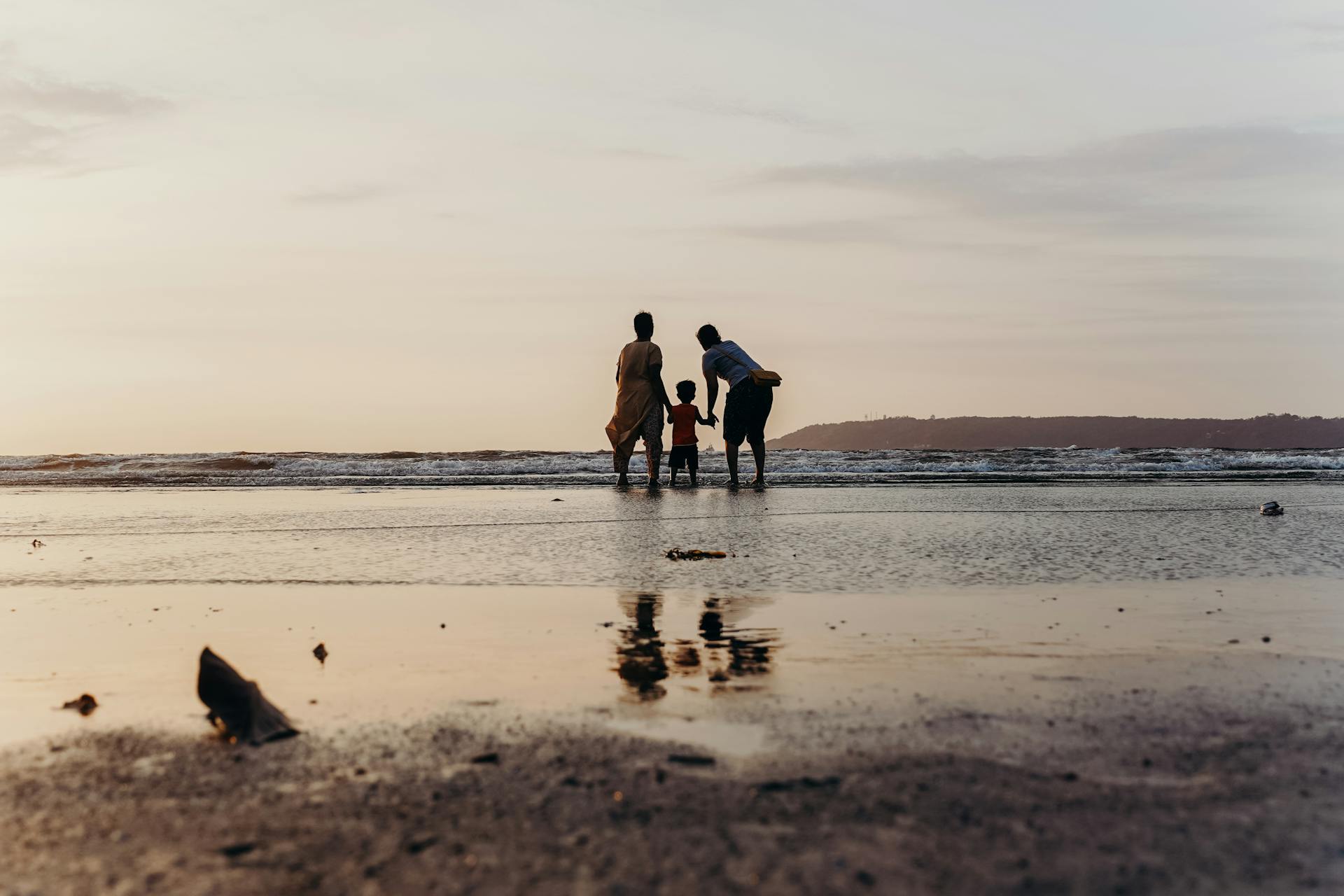 A family enjoys bonding time at the beach during a serene sunset, holding hands by the ocean's edge.