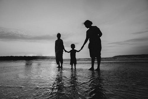 Monochrome Photo of People Holding Hands While Standing on Beach