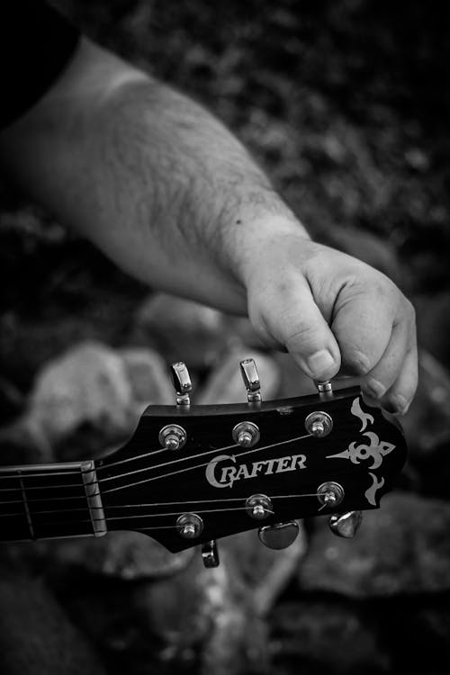 Grayscale Photo of Person Tuning His Guitar