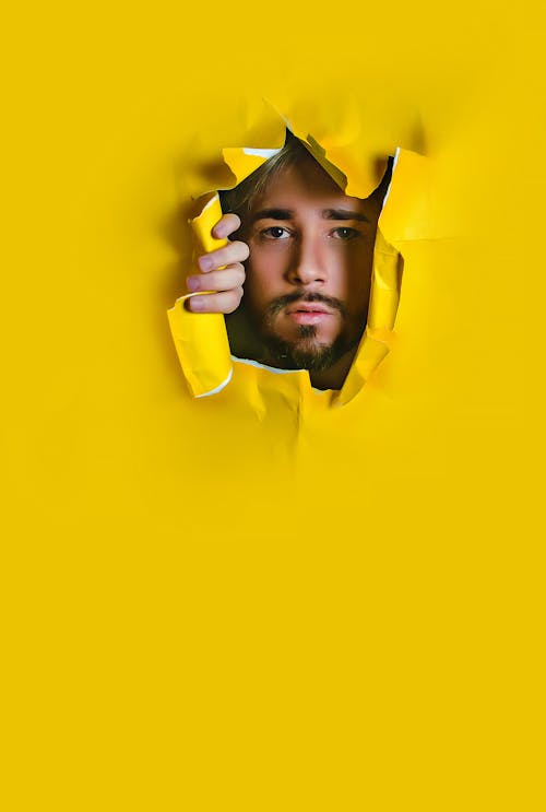 Photo of a Man Looking Through a Hole in a Yellow Paper