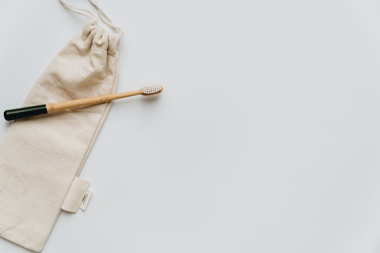 Composition Of Soft Bag With Wooden Toothbrush On White Surface