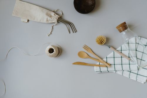 Free From above of composition of wooden cutlery with transparent bottle near dish washing brush on kitchen table and ball of threads near stainless eco straws on white surface Stock Photo
