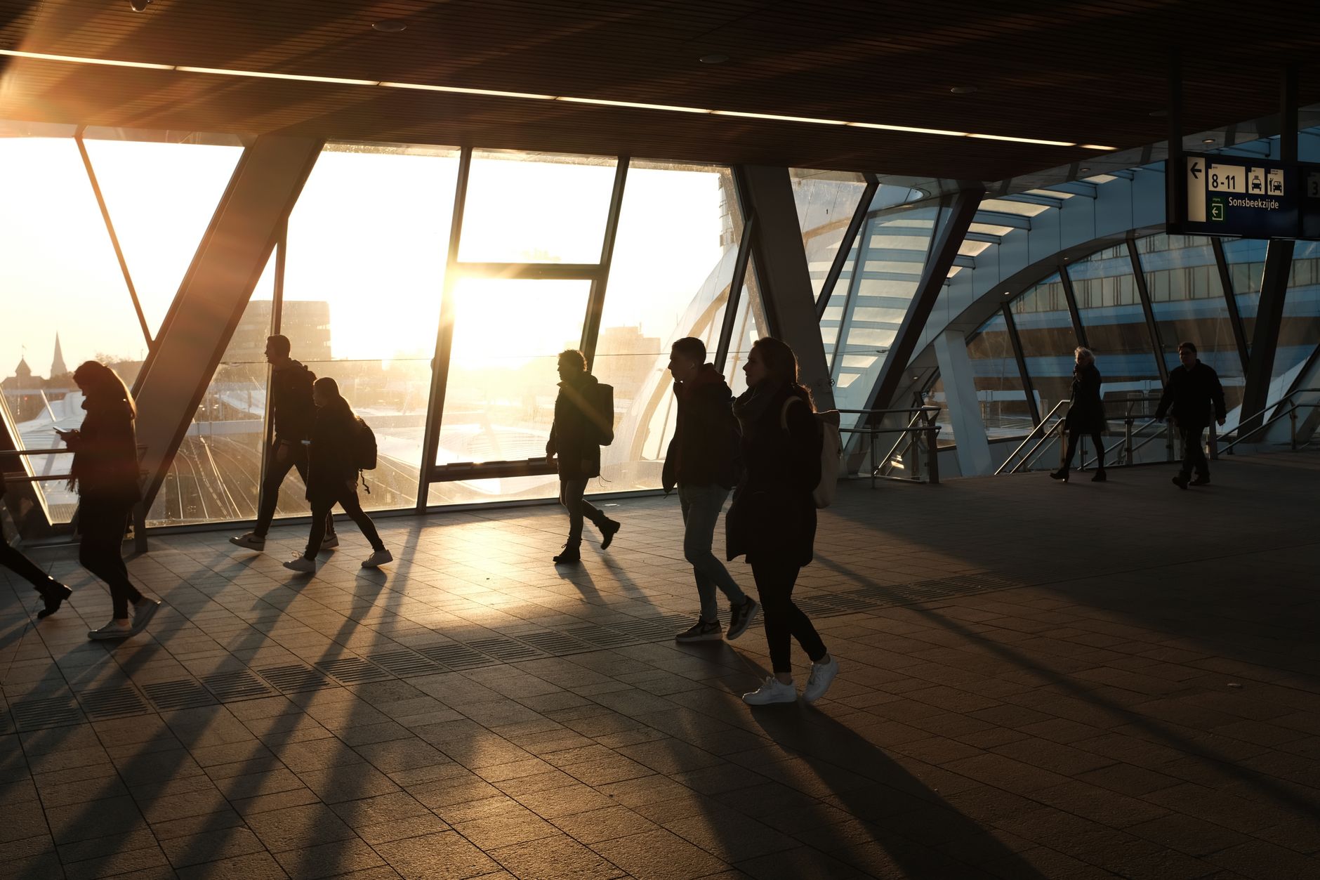 早上自然醒更穩定:光線與作息實用技巧 Commuters silhouetted against sunrise light in a modern train station, capturing the essence of daily routine.