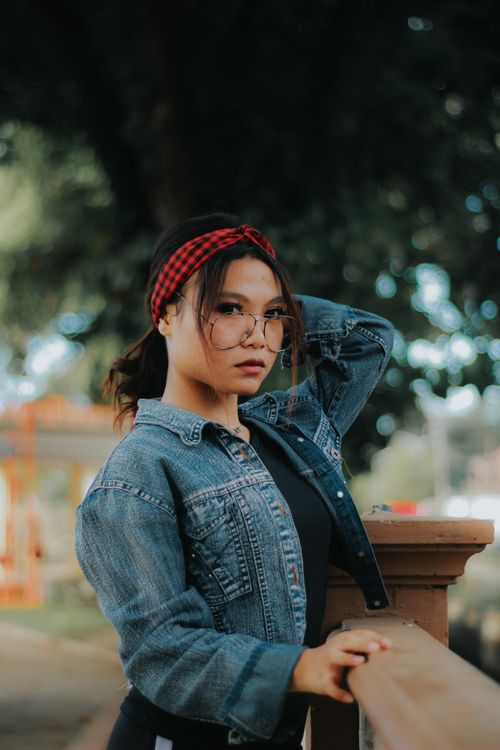 Free Portrait of a woman in a denim jacket with eyeglasses posing outdoors. Stock Photo