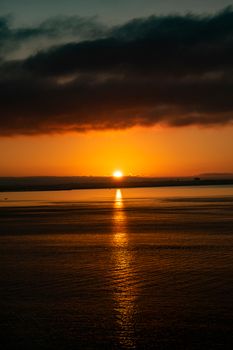 Picturesque view of rippled ocean illuminated by sun near mounts under cloudy sky at colorful sundown at dusk