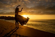 日落时分，一名女子在沙滩上优雅起舞，她的身影映衬着大海，勾勒出令人惊叹的轮廓