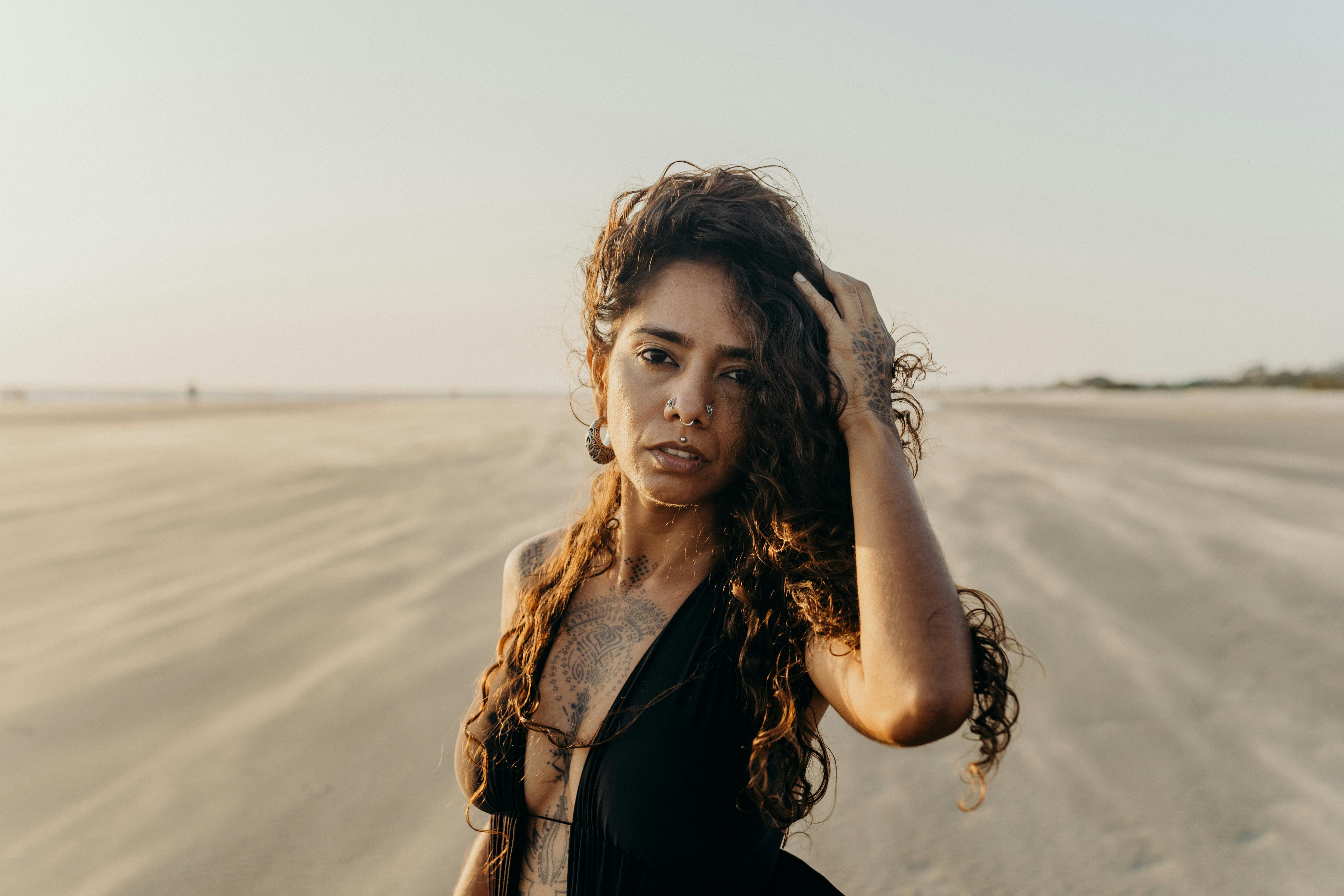 日落时分，一位有纹身的沉思的年轻女子站在沙滩上，捕捉到了一个宁静的时刻