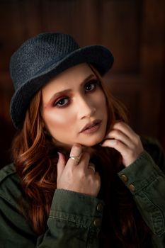 From above of young feminine female with makeup in ring and trendy hat touching face while looking at camera
