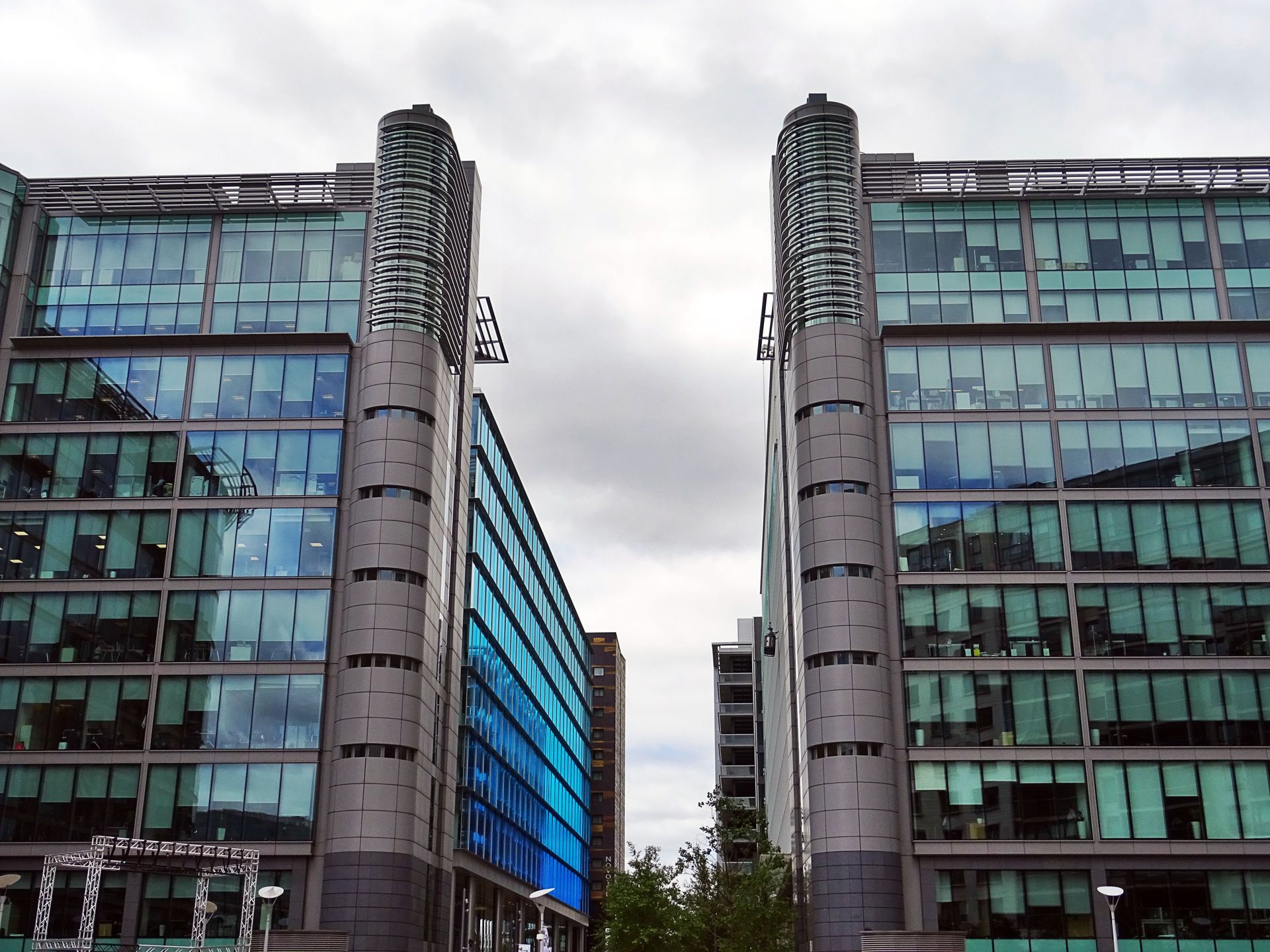 Urban cityscape featuring modern skyscrapers with a reflective glass facade under a cloudy sky.