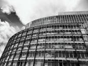 这张黑白照片里，一座现代摩天大楼矗立在多云天空下，玻璃窗反射着光线