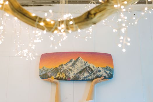 Hands holding a colorful mountain art piece against a lit backdrop, evoking creativity and celebration.