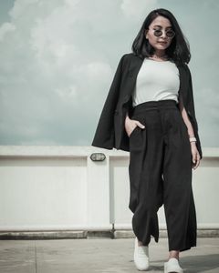 Low angle of young ethnic lady in trendy wear and sneakers walking with hand in pocket under cloudy sky and looking down