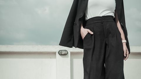 Low angle of young ethnic lady in trendy wear and sneakers walking with hand in pocket under cloudy sky and looking down