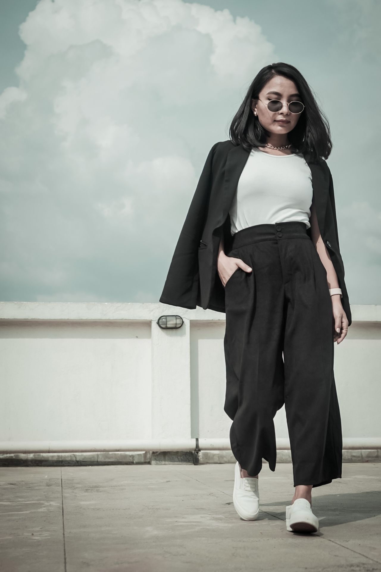 Woman in a black blazer, white tee, and black wide-leg trousers with white sneakers