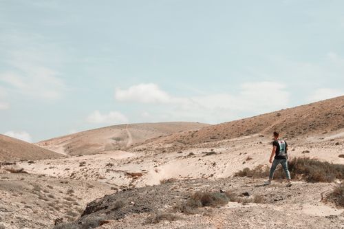 Free A man in a black shirt walks through an arid desert landscape under a clear blue sky. Stock Photo