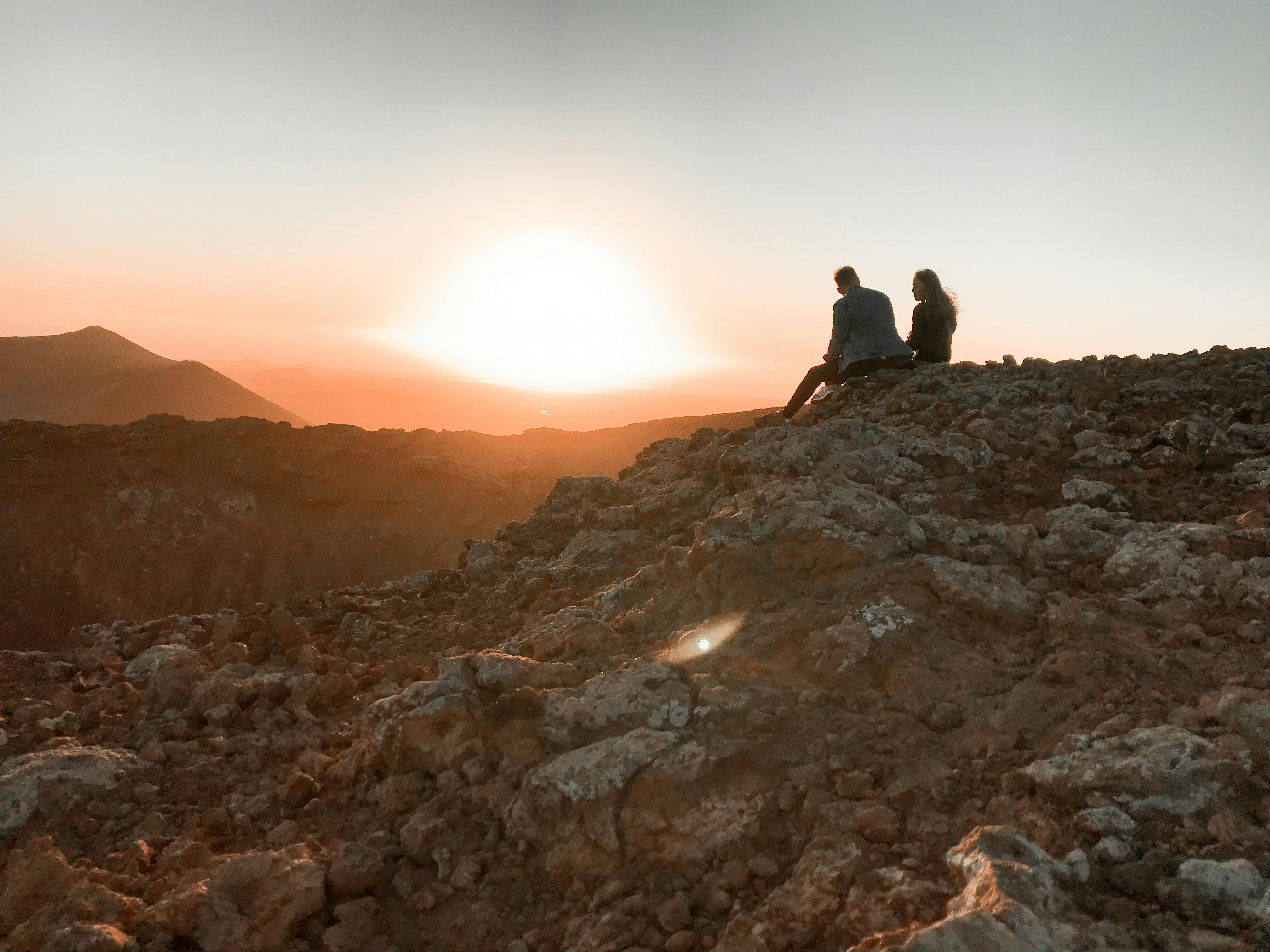 a man and woman sitting on rock during sunset