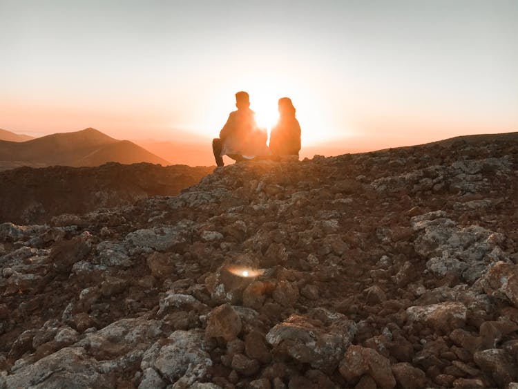 A Couple Sitting On Rocky Mountain During Sunset