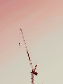 A tall tower crane silhouetted against a pastel sunset sky in Central Visayas, Philippines.