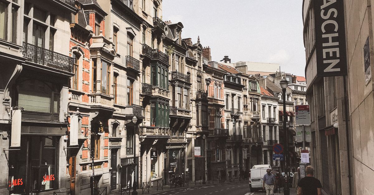 Quaint street in Brussels, Belgium, featuring historic architecture under a bright sky with pedestrians and cars.