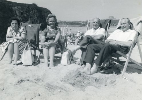 Retro photo of couples sitting on a beach enjoying the sun in deckchairs.