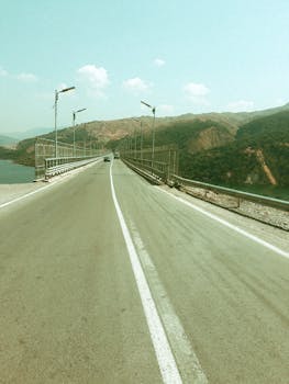 A long highway bridge stretches over a scenic landscape with mountains and a river under a clear sky.