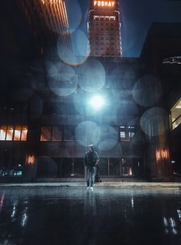 A man stands in the rain at night near the illuminated Foshay Tower in Minneapolis.