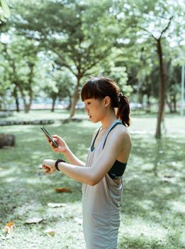 一位健康的年轻女子在宁静的公园里，拿着智能手机查看她的智能手表