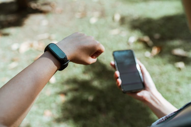 Crop Faceless Person Showing Smart Watch While Using Smartphone Outdoors