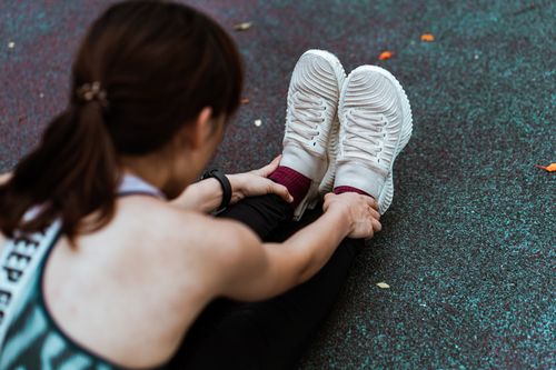 Free Top view of crop unrecognizable female athlete in sports clothes and sneakers doing forward bend while sitting on asphalt footpath with shabby surface Stock Photo