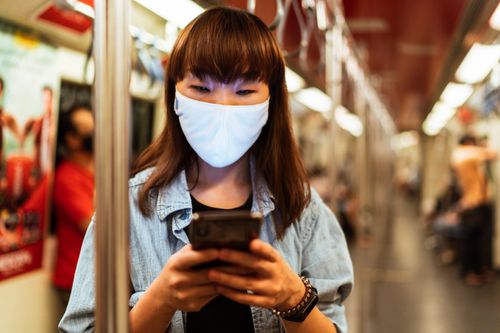 Free Asian woman in denim jacket texting on smartphone while wearing a face mask on public transport. Stock Photo