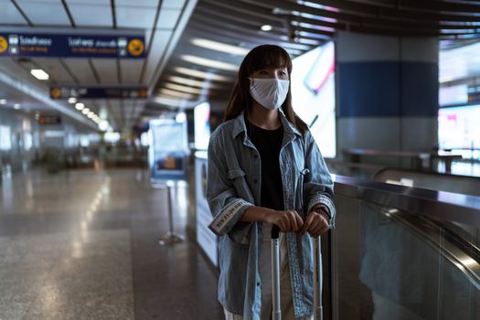 一名穿着牛仔夹克、戴着口罩的亚洲女子在车站拿着行李，等待出行