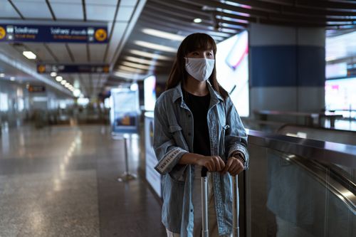 Free Asian woman in denim jacket and face mask holding luggage in a station, waiting for travel. Stock Photo