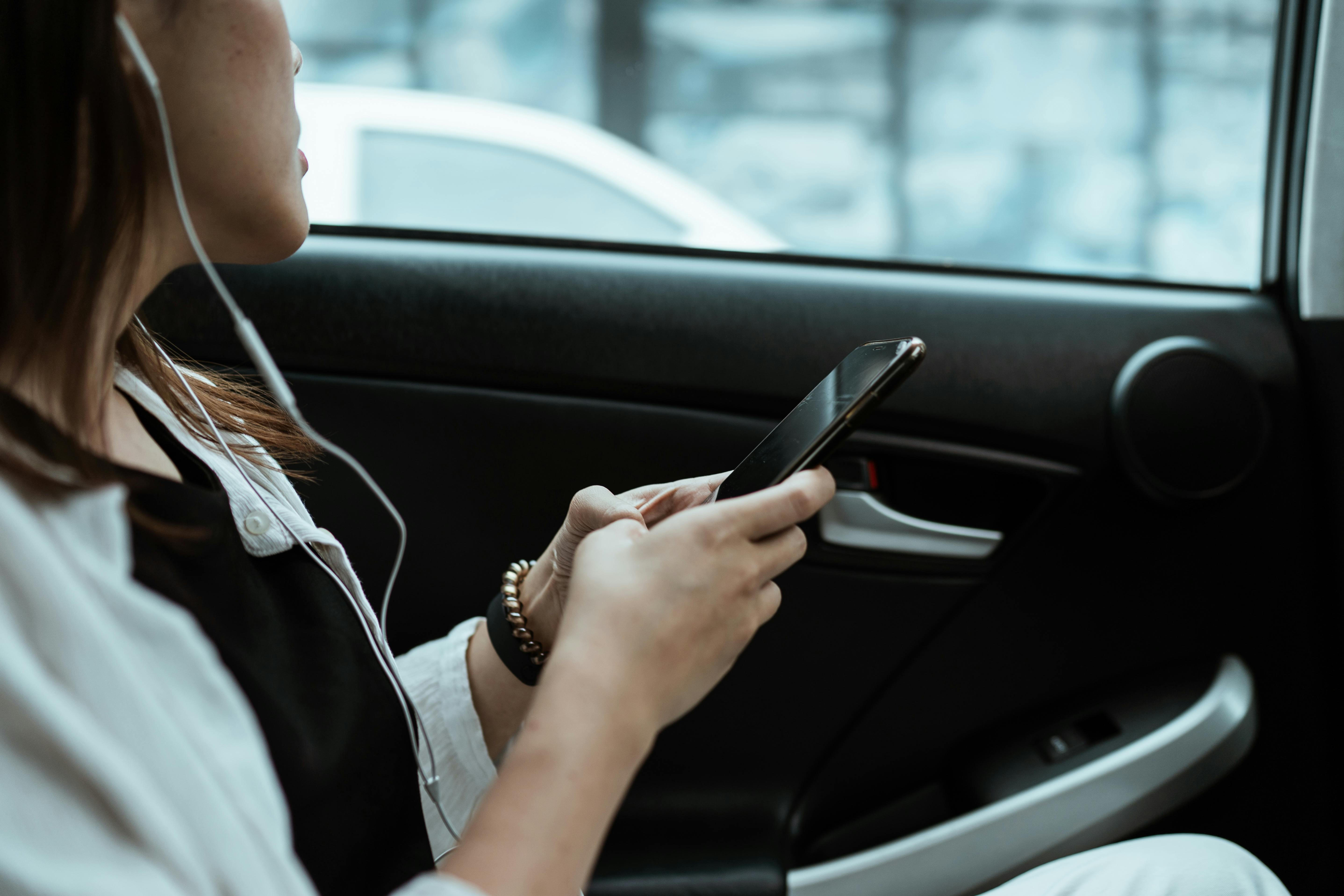 crop unrecognizable woman listening to music on smartphone in car