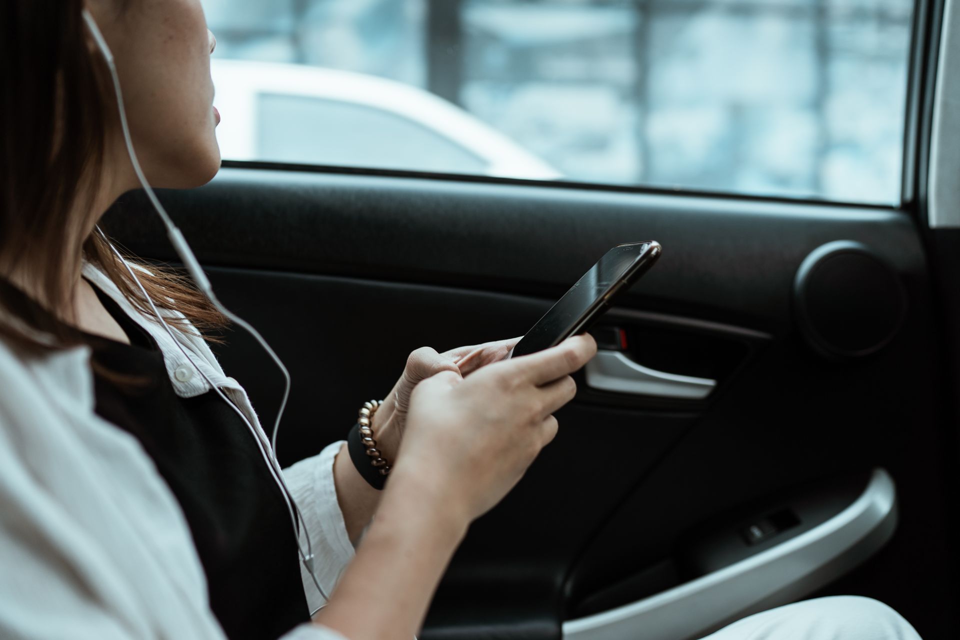 Woman listening to music and using a smartphone during a car ride, enjoying leisure time.