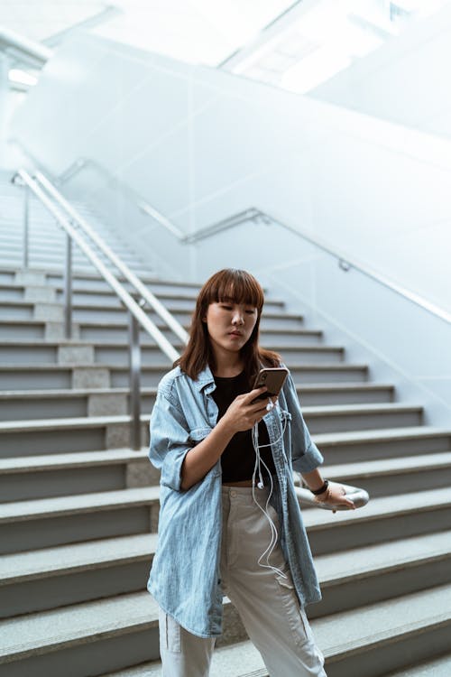 Free Woman Holding a Handrail and Using her Smartphone Stock Photo