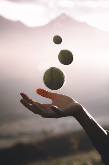 Crop faceless female throwing tennis balls into air while standing on field in countryside on sunny day