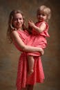 Side view of happy female teenager in romantic dress hugging adorable little sister and looking at camera