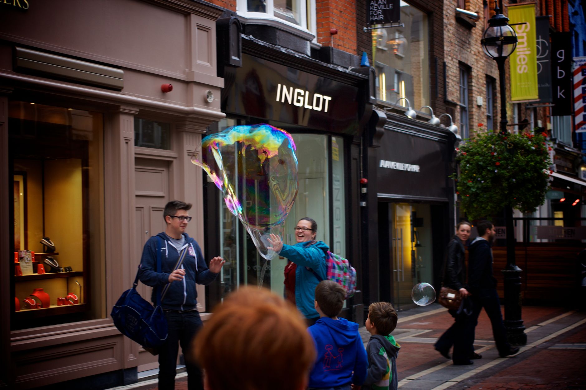 Playful scene in a city street with people enjoying a giant soap bubble.